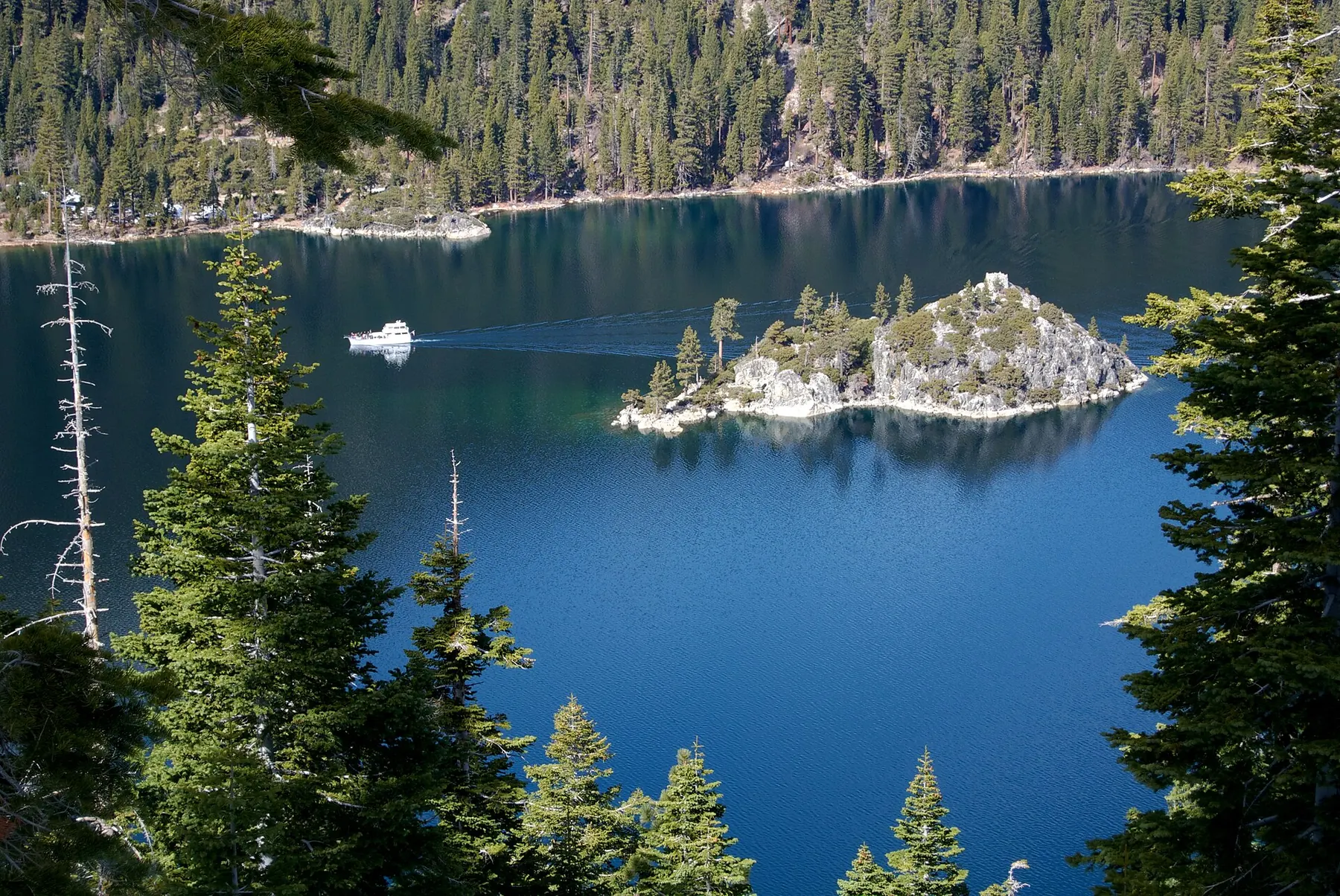 Fannette Island, a small rocky island with pines, in the deep blue water of Emerald Bay, with a white boat passing and forested slopes behind