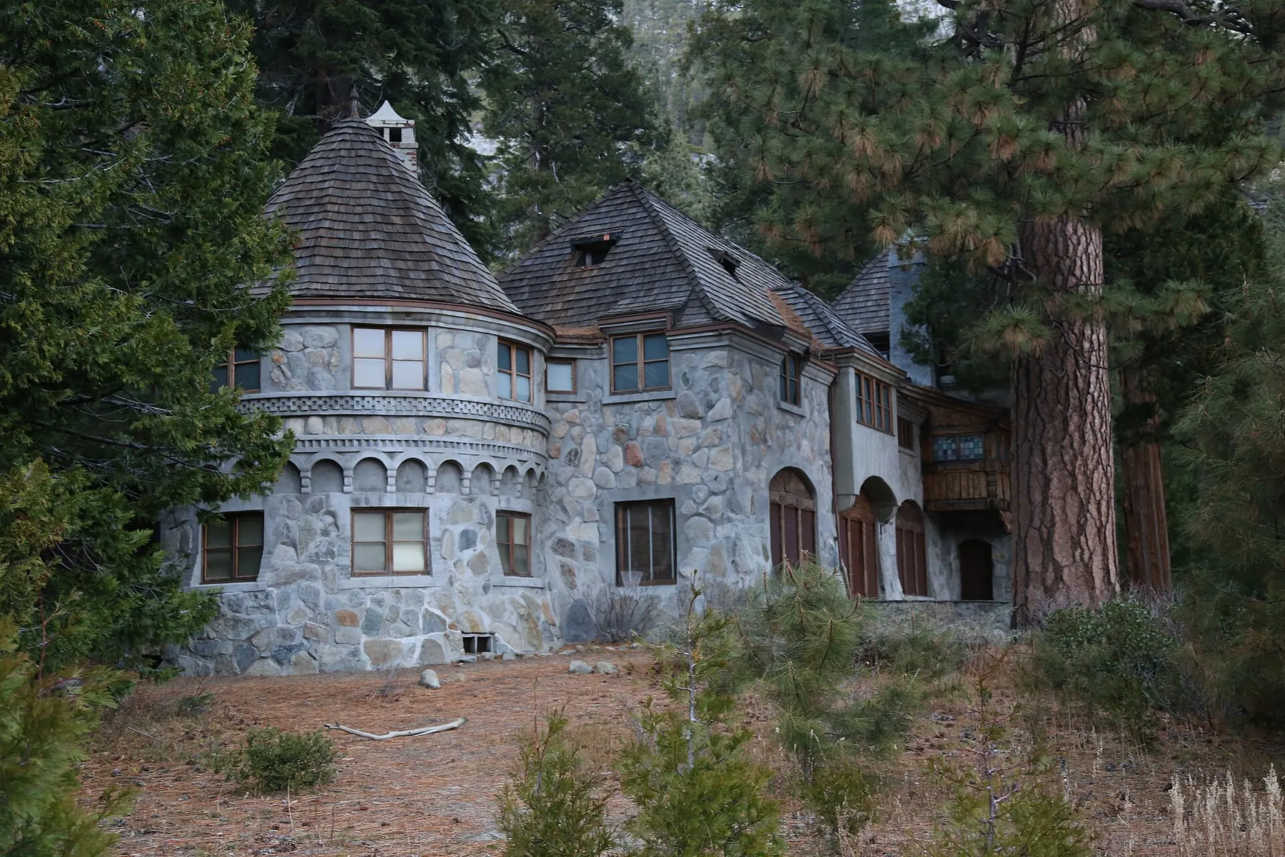 The grey stone Vikingsholm mansion with shingled turrets standing among tall pines on the shore of Emerald Bay